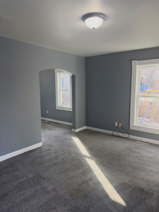 unfurnished room featuring arched walkways, carpet flooring, and baseboards