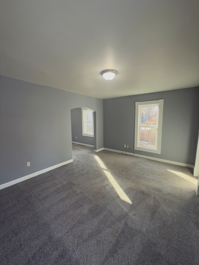 empty room with baseboards, carpet, and arched walkways