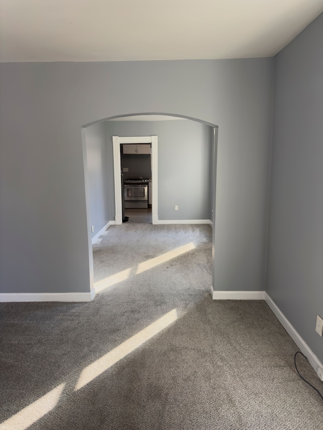 carpeted empty room with arched walkways and baseboards