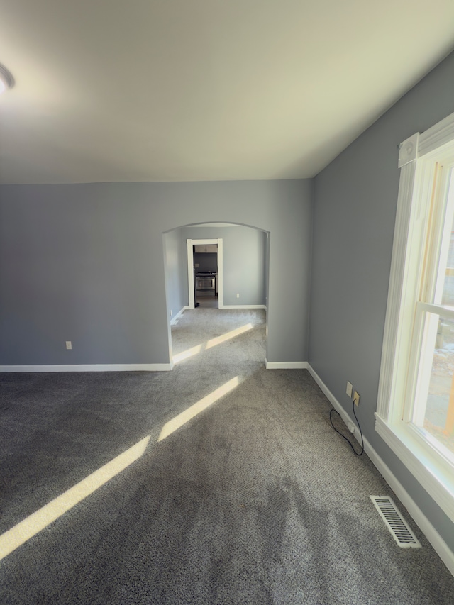 empty room featuring visible vents, baseboards, carpet, and arched walkways