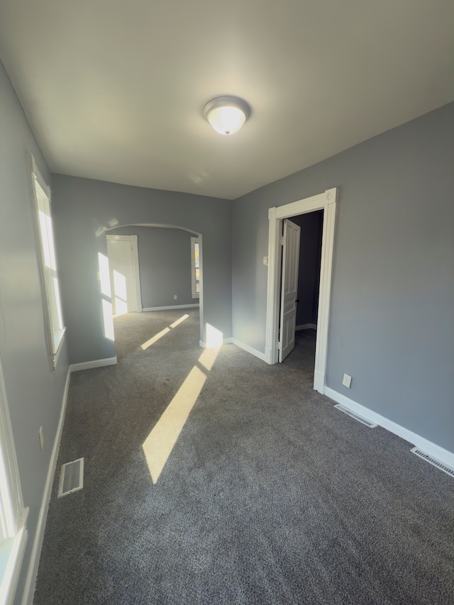 spare room featuring arched walkways, visible vents, baseboards, and dark colored carpet