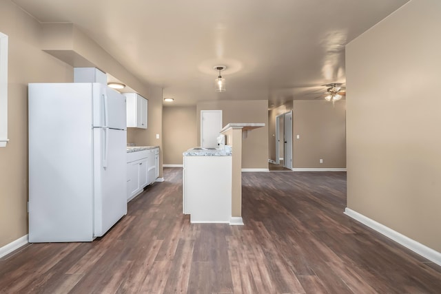 kitchen featuring dark wood-style flooring, a ceiling fan, freestanding refrigerator, white cabinets, and baseboards