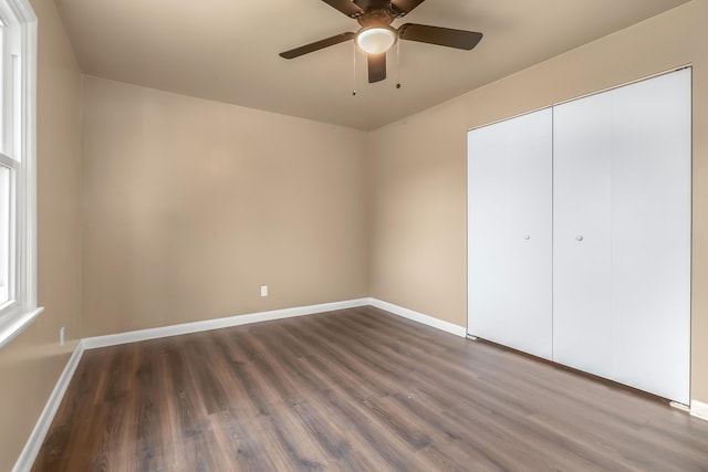 unfurnished bedroom with dark wood-style floors, ceiling fan, a closet, and baseboards