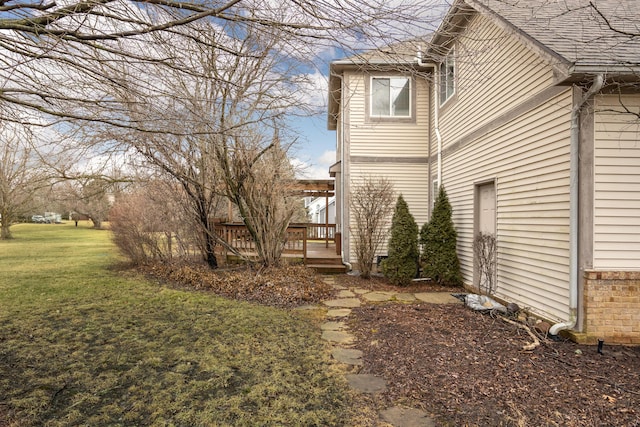 view of side of property featuring roof with shingles, a yard, and a deck