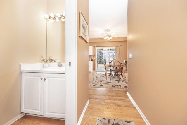 hallway featuring light wood finished floors, a sink, and baseboards