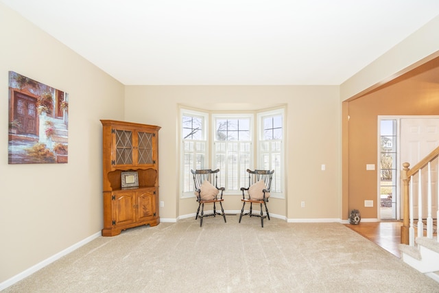 living area with baseboards, stairway, and light colored carpet