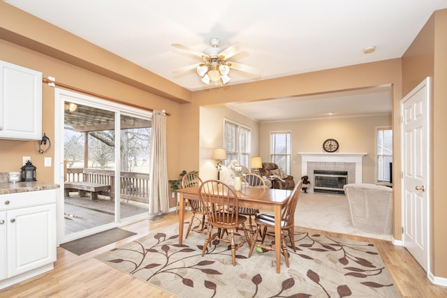 dining space with light wood-type flooring, a ceiling fan, and a tile fireplace