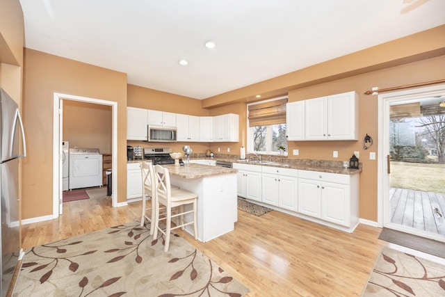 kitchen with a center island, a breakfast bar area, appliances with stainless steel finishes, white cabinets, and independent washer and dryer