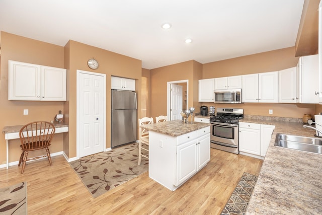 kitchen featuring a center island, light wood finished floors, appliances with stainless steel finishes, built in study area, and a sink