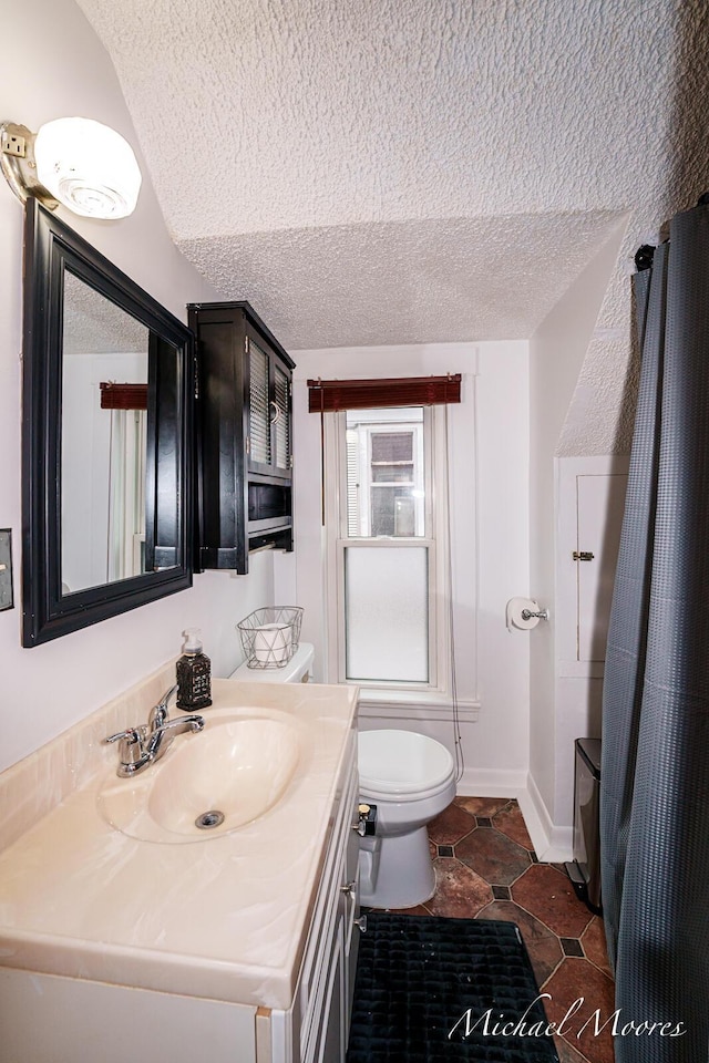 bathroom with a textured ceiling, toilet, vanity, and baseboards