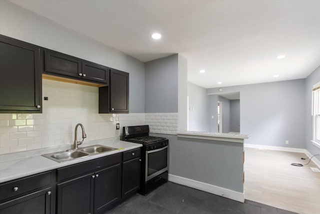 kitchen with tasteful backsplash, light countertops, a sink, and stainless steel gas range oven