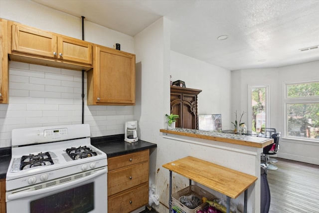 kitchen with white range with gas stovetop, wood finished floors, visible vents, baseboards, and backsplash