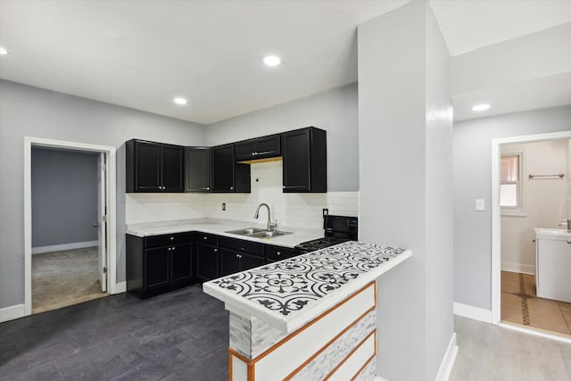 kitchen featuring light countertops, black gas range, decorative backsplash, a sink, and dark cabinetry