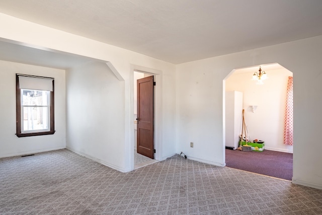 carpeted empty room featuring baseboards, visible vents, arched walkways, and an inviting chandelier