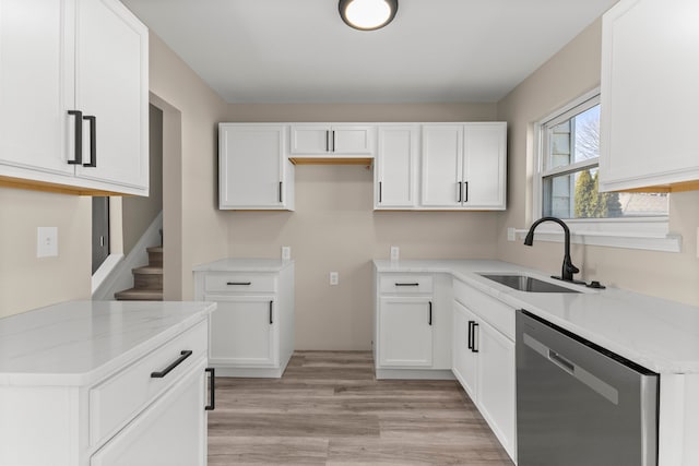 kitchen with light stone countertops, white cabinetry, a sink, stainless steel dishwasher, and light wood-type flooring