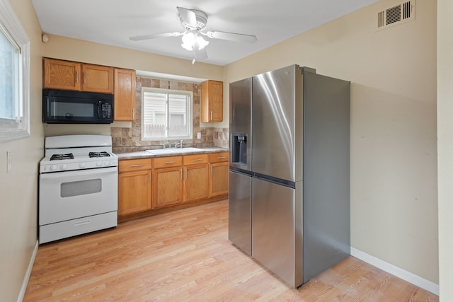 kitchen featuring stainless steel fridge, visible vents, white gas range, black microwave, and a sink