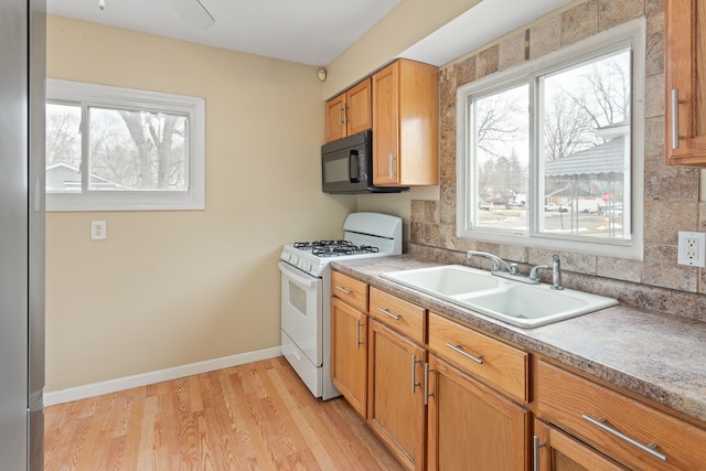 kitchen featuring light wood finished floors, a sink, black microwave, baseboards, and white gas range oven