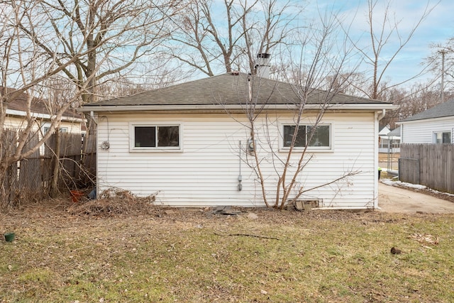 back of house featuring roof with shingles, fence, a chimney, and a lawn