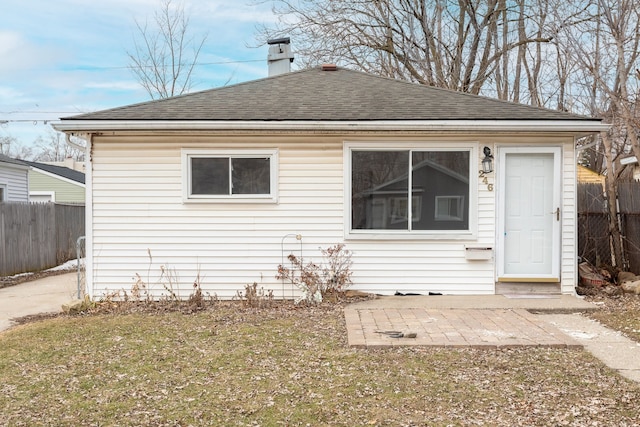 view of front of home featuring a patio area, roof with shingles, fence, and a chimney