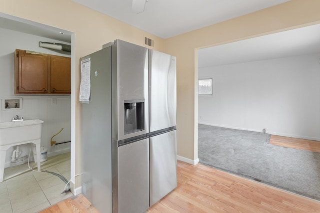 kitchen featuring baseboards, visible vents, light colored carpet, stainless steel fridge with ice dispenser, and brown cabinets