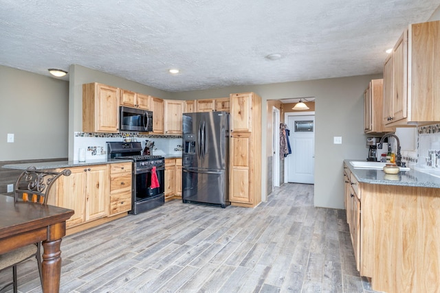 9915 85th Ave, Mecosta, MI 49332 - kitchen with black fridge with ice dispenser, light brown cabinetry, stainless steel microwave, a sink, and gas stove