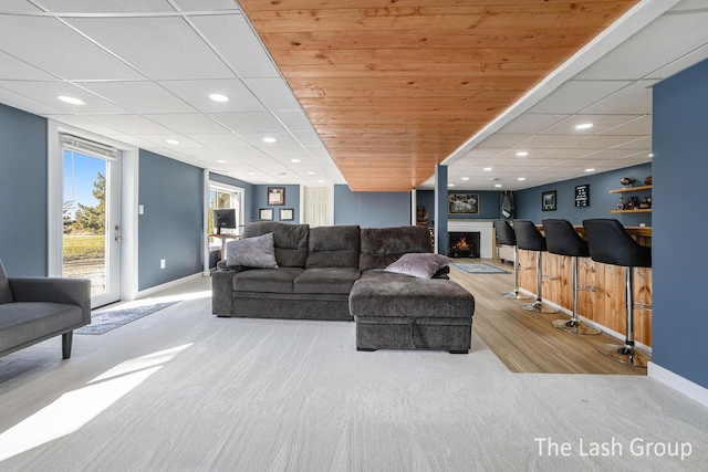 living area with recessed lighting, a bar, a drop ceiling, a lit fireplace, and baseboards