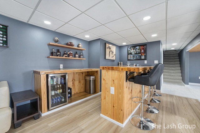 bar featuring recessed lighting, beverage cooler, stairs, light wood-type flooring, and a bar