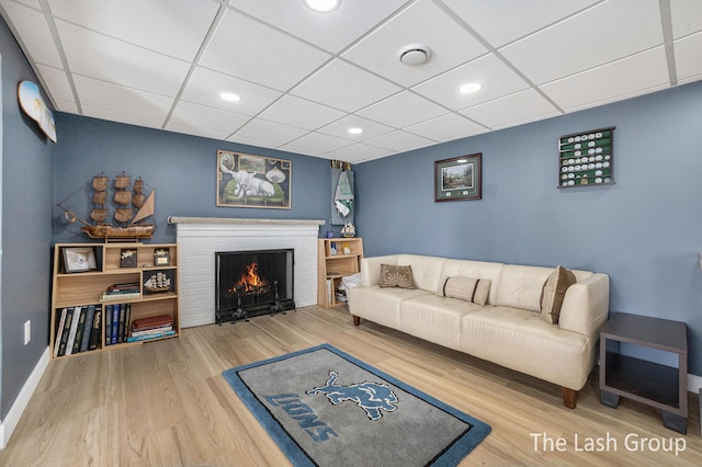 living area featuring a drop ceiling, recessed lighting, a fireplace, wood finished floors, and baseboards