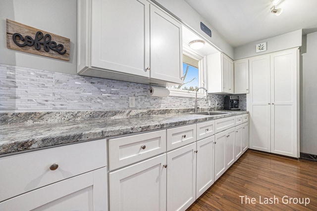 kitchen with tasteful backsplash, white cabinets, a sink, and dark wood-type flooring