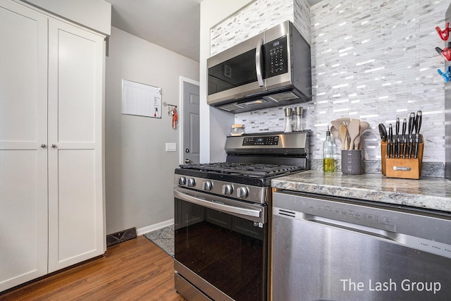 kitchen with backsplash, appliances with stainless steel finishes, white cabinets, wood finished floors, and baseboards