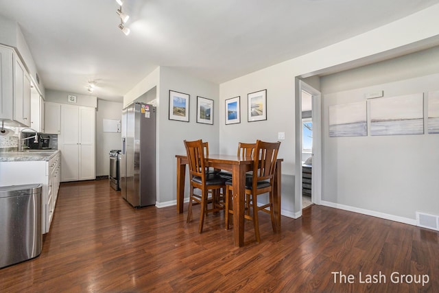 dining room with dark wood-type flooring, track lighting, visible vents, and baseboards