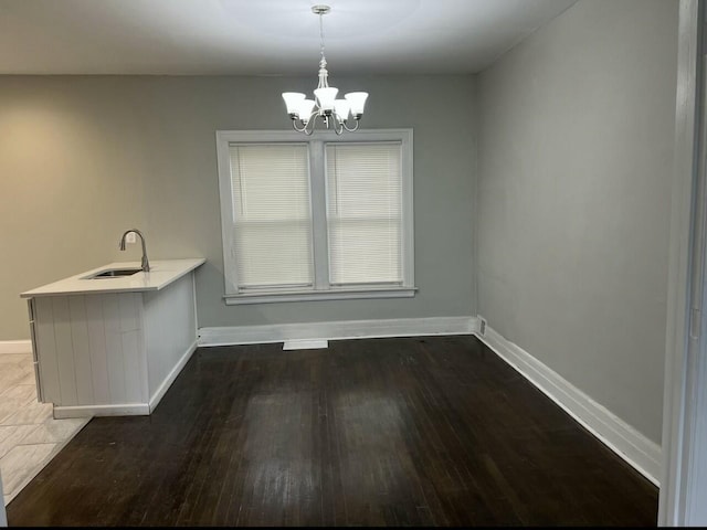 unfurnished dining area with baseboards, dark wood-type flooring, a sink, and a chandelier