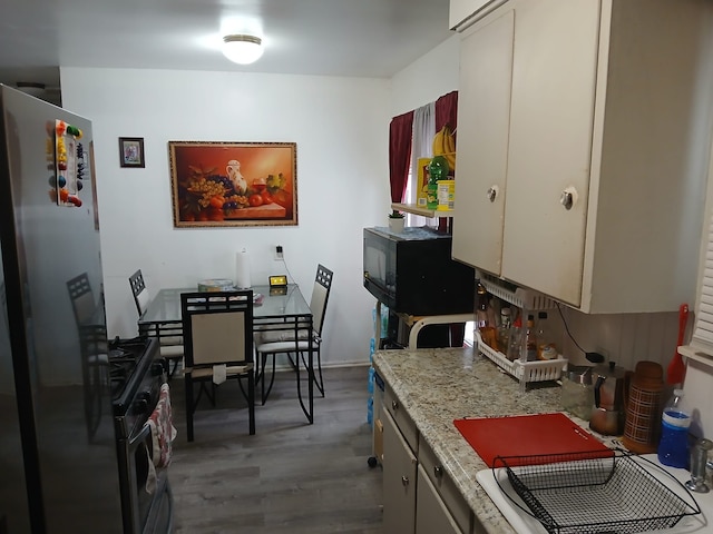 kitchen with light stone counters, wood finished floors, freestanding refrigerator, and gas range oven