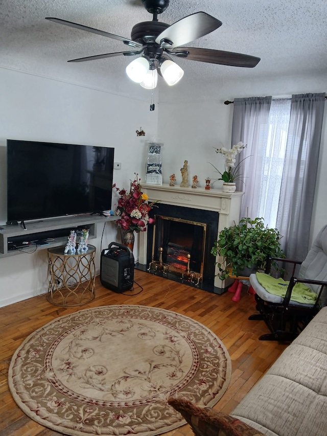 living area featuring a textured ceiling, a lit fireplace, wood finished floors, and a ceiling fan