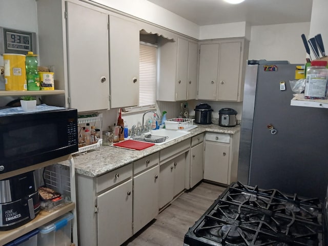 kitchen with black appliances, light countertops, light wood-style floors, and a sink