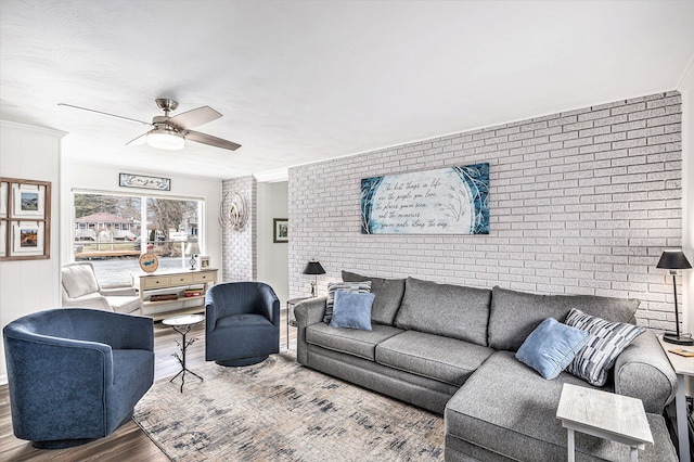 living area with an accent wall, wood finished floors, brick wall, and ceiling fan