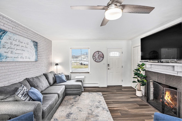 living room featuring brick wall, ceiling fan, dark wood finished floors, a warm lit fireplace, and a baseboard radiator