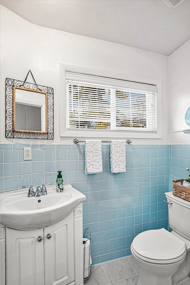 half bathroom featuring vanity, tile walls, and toilet