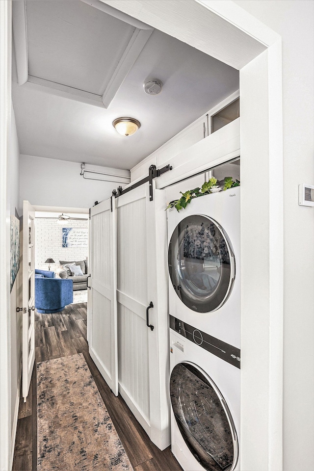 laundry room with laundry area, stacked washing maching and dryer, a barn door, and dark wood-style flooring