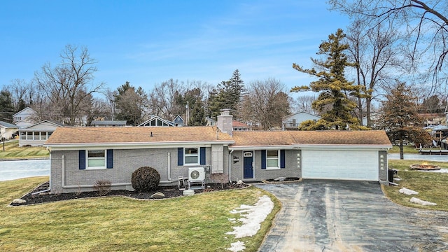 view of front facade featuring brick siding, a front lawn, a chimney, a garage, and driveway