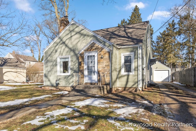 view of front facade featuring an outdoor structure, fence, a detached garage, driveway, and a chimney