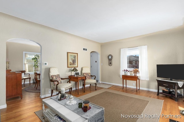 living room with light wood finished floors, visible vents, arched walkways, and baseboards