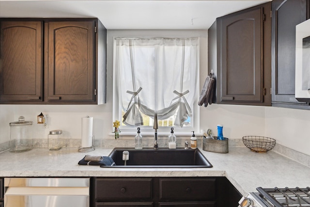 kitchen with dark brown cabinetry, stainless steel appliances, light countertops, and a sink