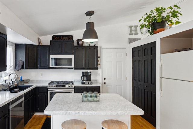 kitchen with stainless steel appliances, light countertops, vaulted ceiling, a sink, and a kitchen island