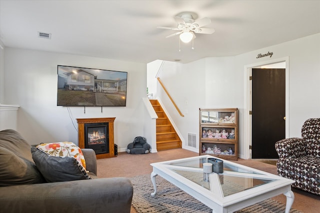 living area featuring a glass covered fireplace, visible vents, carpet flooring, and stairs