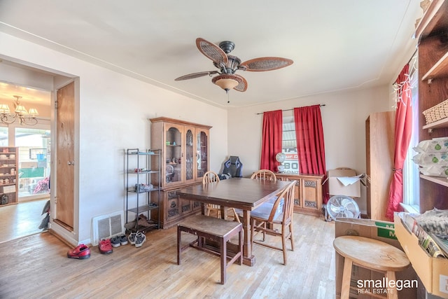 dining space with ceiling fan with notable chandelier, visible vents, and light wood-style floors