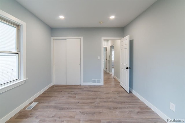 unfurnished bedroom featuring visible vents, baseboards, a closet, and wood finished floors