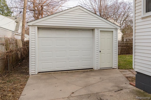 detached garage featuring concrete driveway and fence