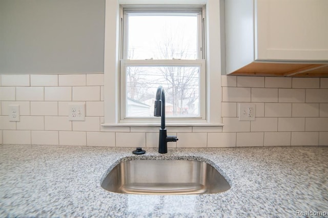 interior details featuring backsplash, light stone countertops, white cabinetry, and a sink