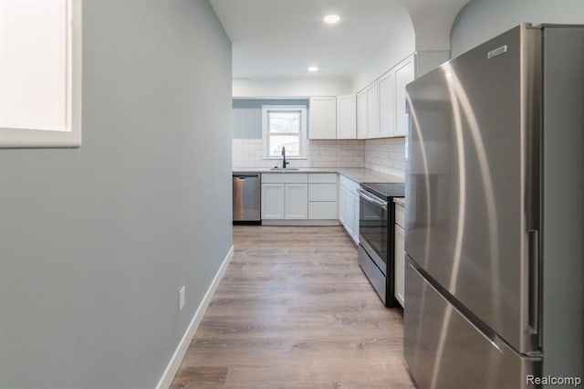 kitchen featuring tasteful backsplash, baseboards, appliances with stainless steel finishes, white cabinetry, and a sink